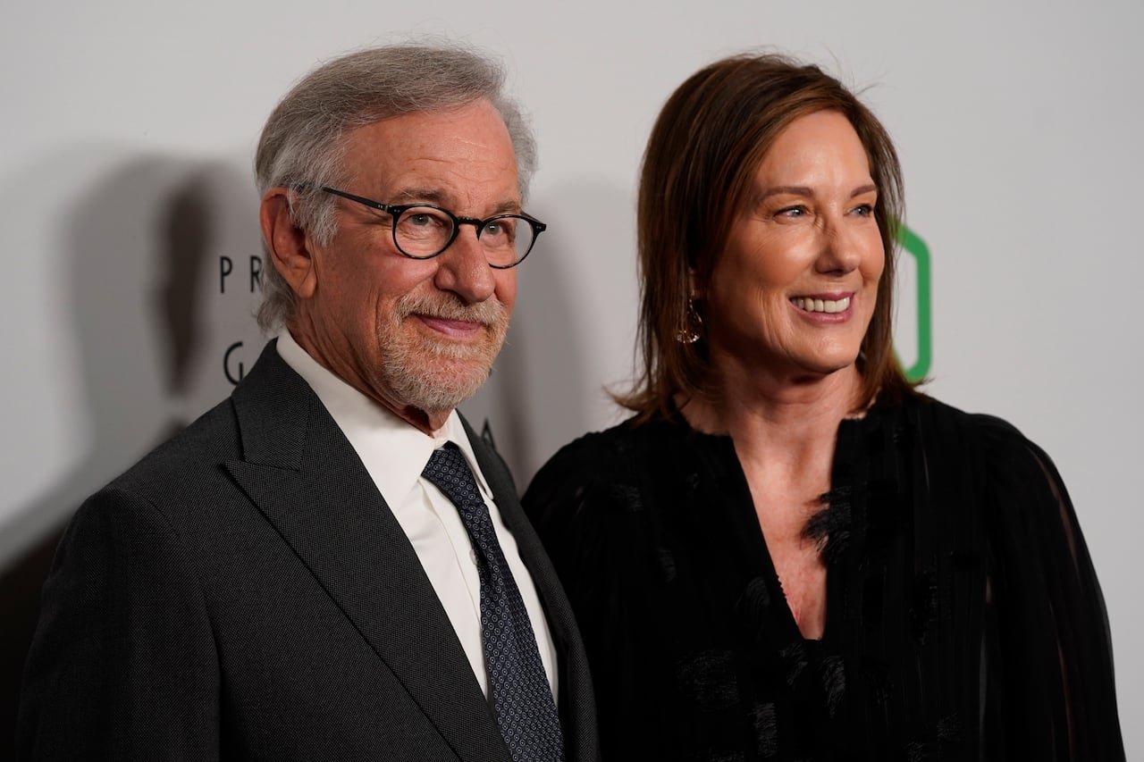 A man and a woman in dark suits stand smiling, looking off-camera to the right.