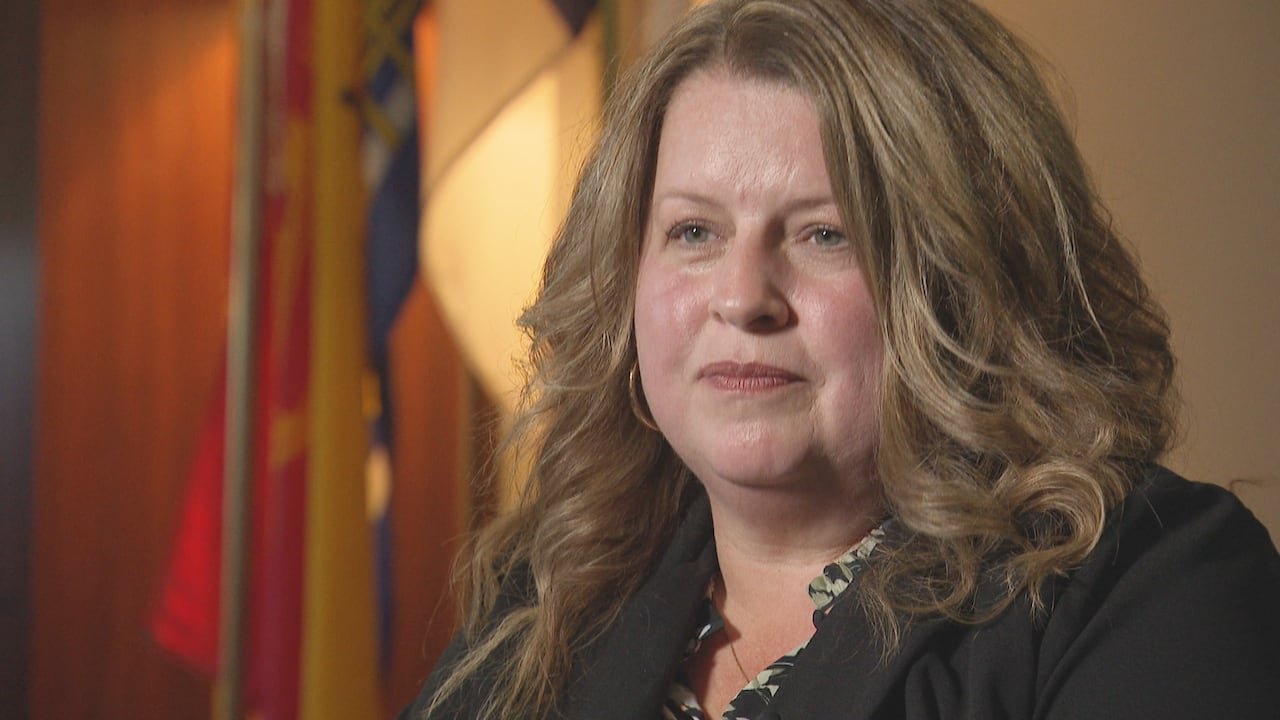 Woman with brown hair stands in front of flags.