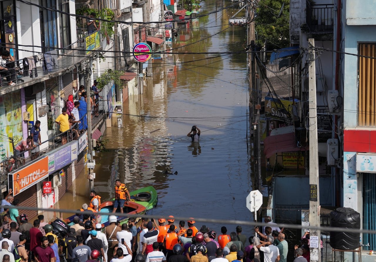 A man wades through a flooded street as people watch from buildings