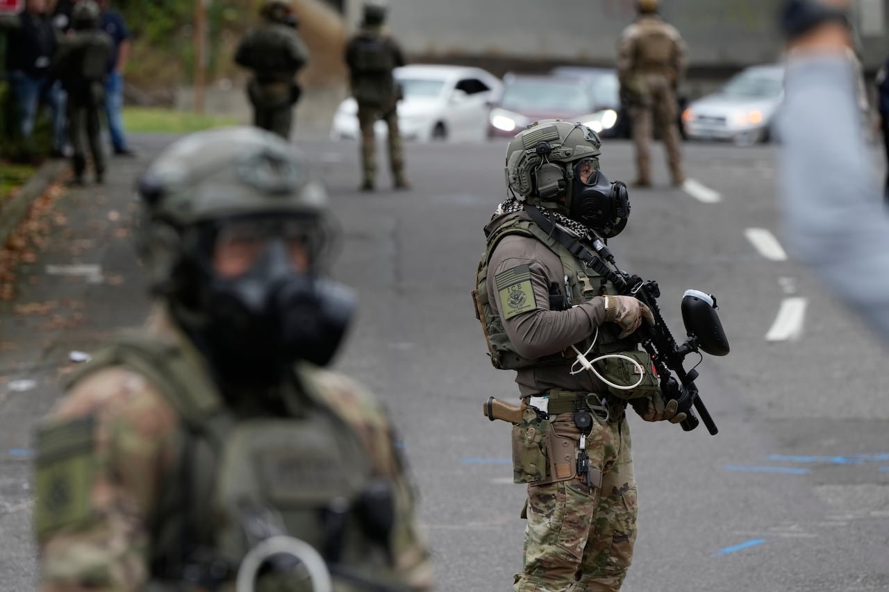 Masked agents who are armed are shown on a street in military-style dress.