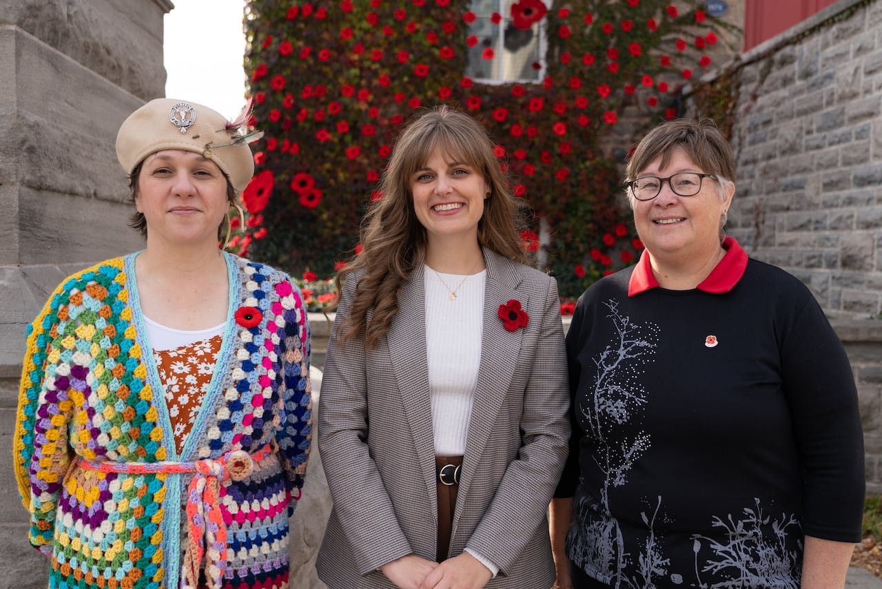 three women standing side by side in front of museum covered in poppies