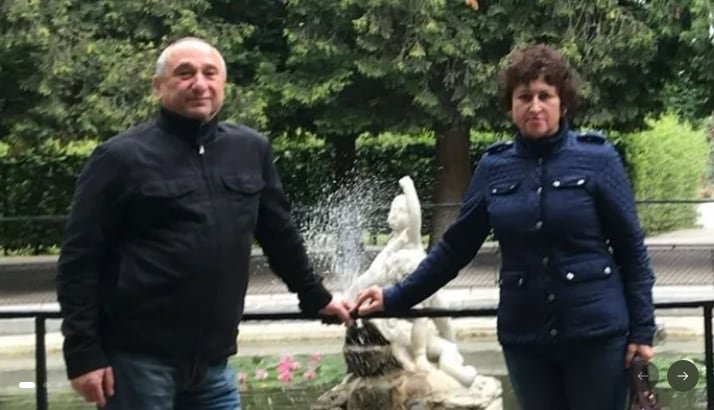An older couple holds hands in front of a fountain