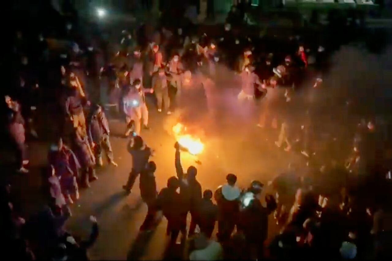 A large group of people gather around a bonfire at night.