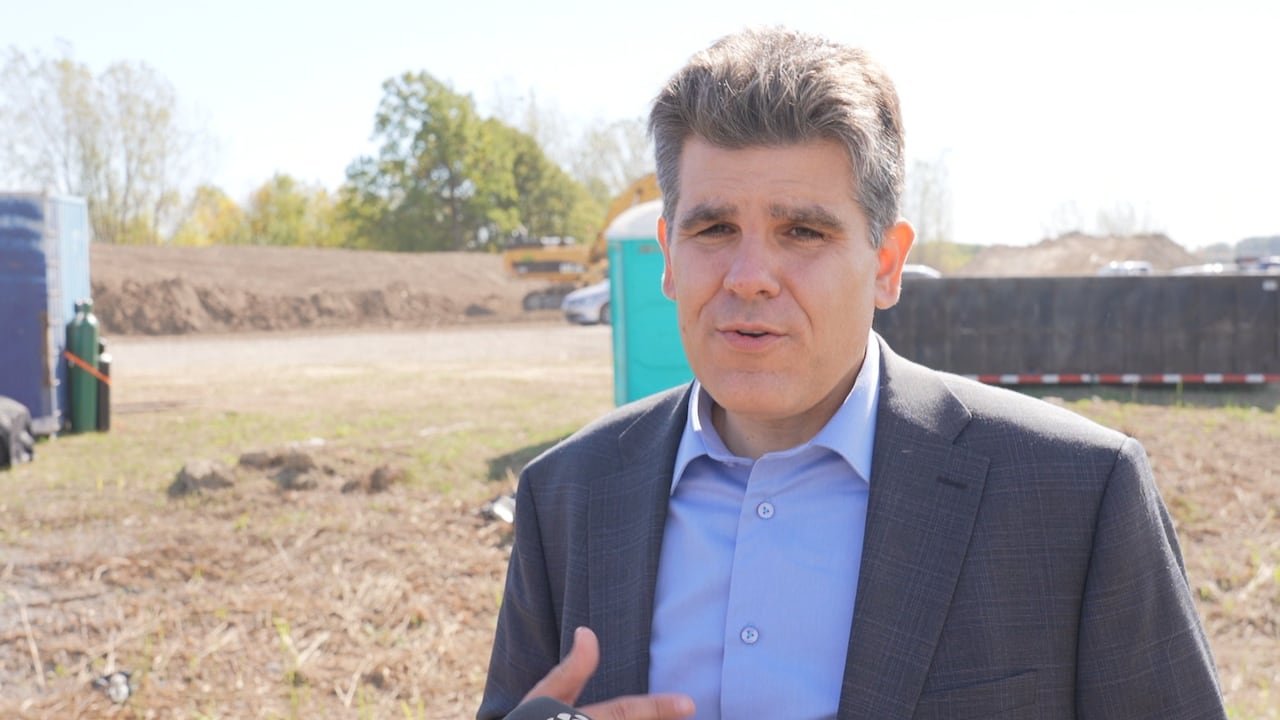 A man in a sport jacket stands at a construction site