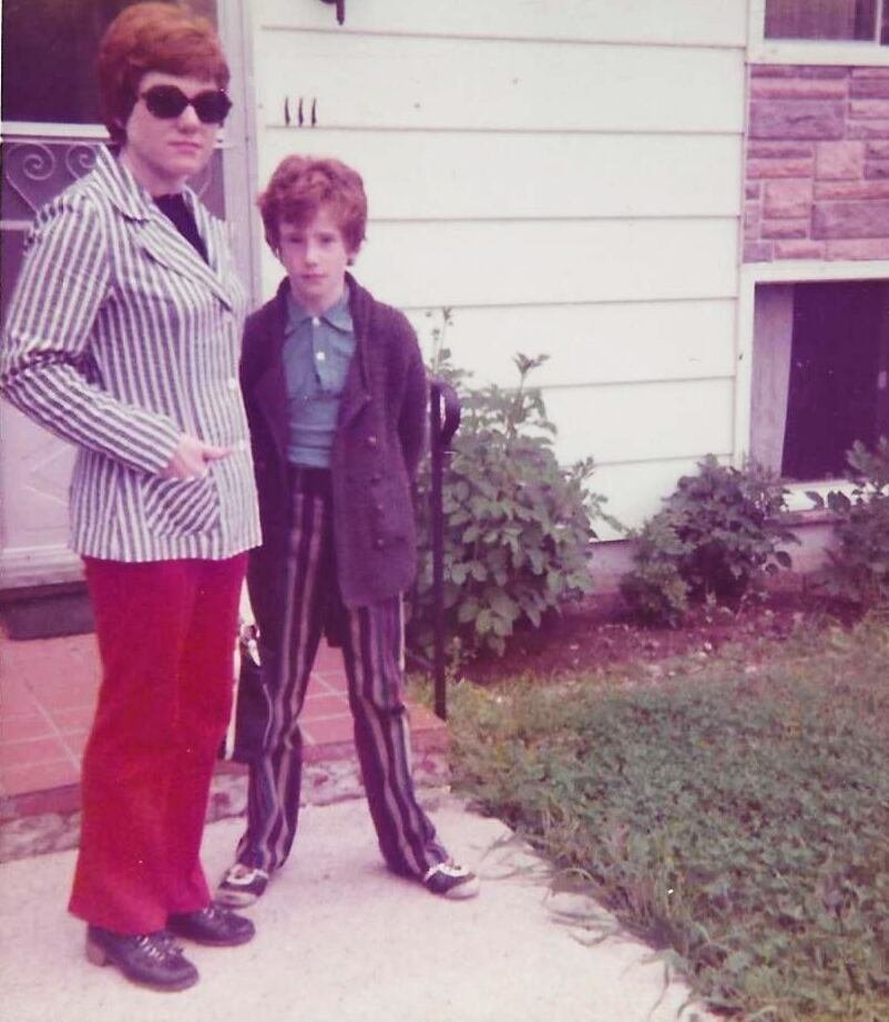 A vintage image of a woman and a young boy standing outside a house door