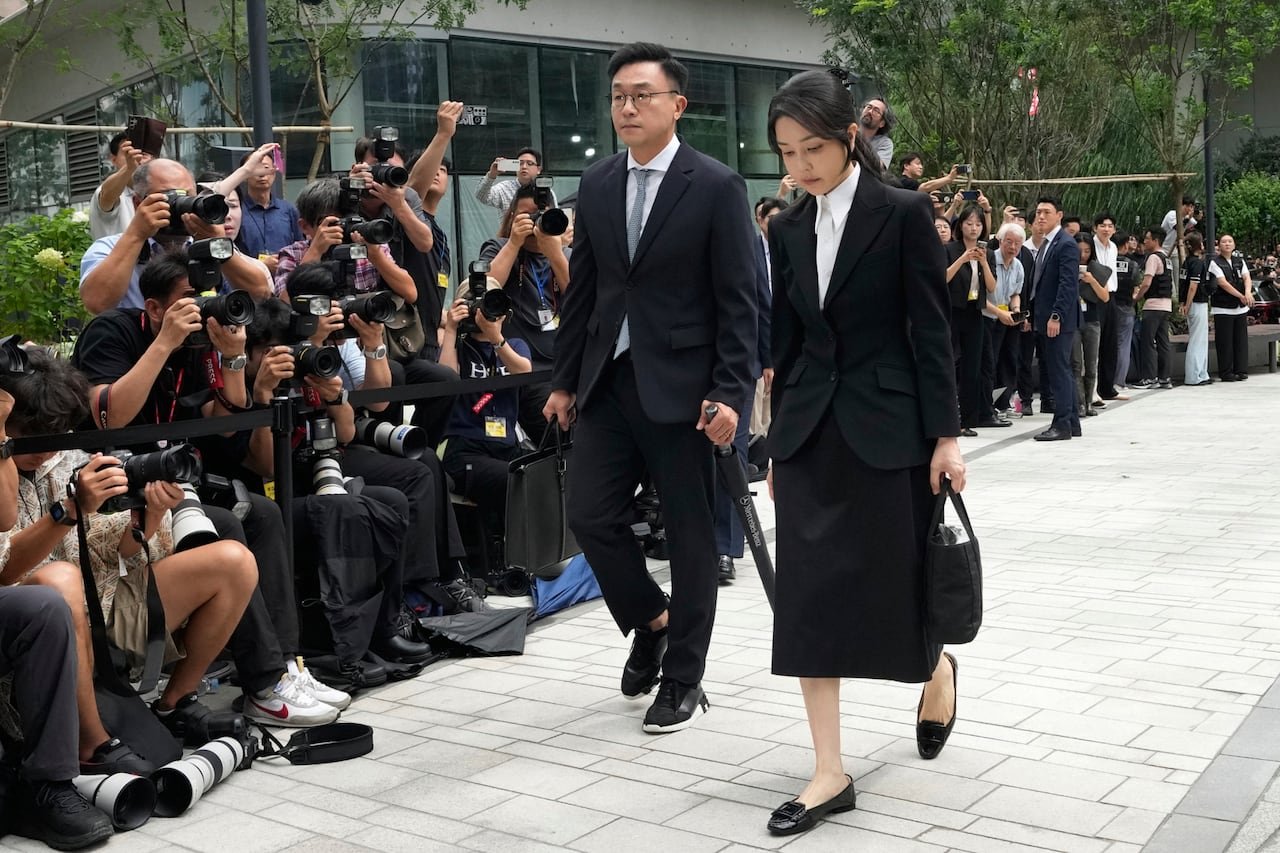 A man and woman walk past a gauntlet of photographers outside a building