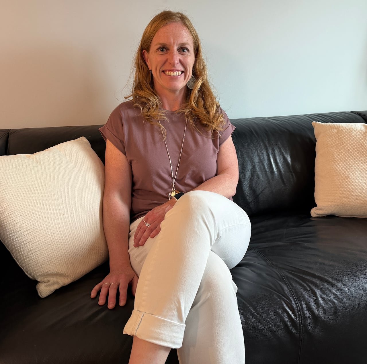 default-253 Woman smiling sitting on a sofa wearing white jeans and a mauve t-shirt.