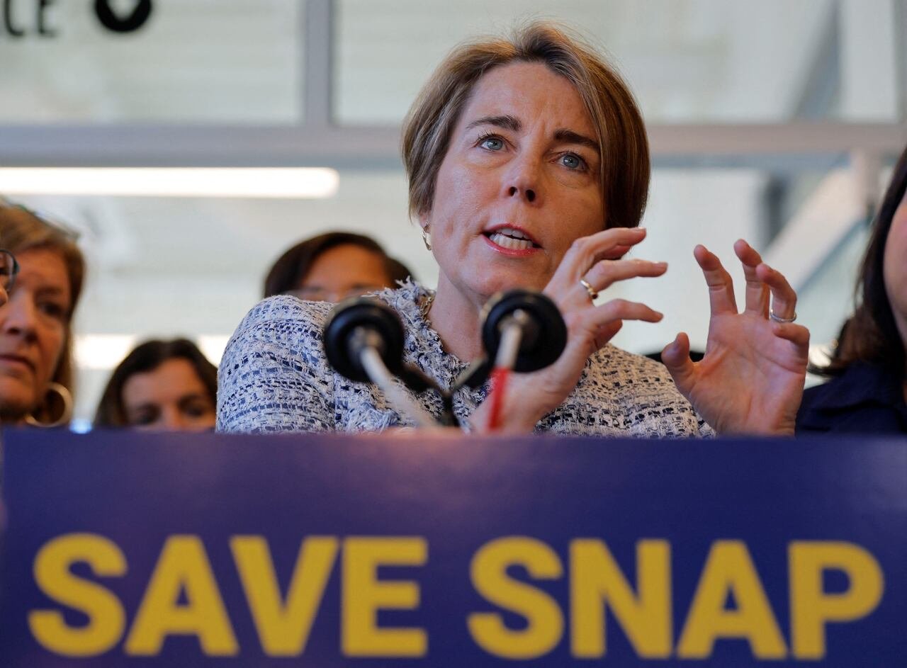default-65 A woman with ear-length hair gestures while speaking at a podium displaying a placard stating, "Save Snap."